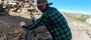 A man in a checked shirt hammers into rocks at an excavation site